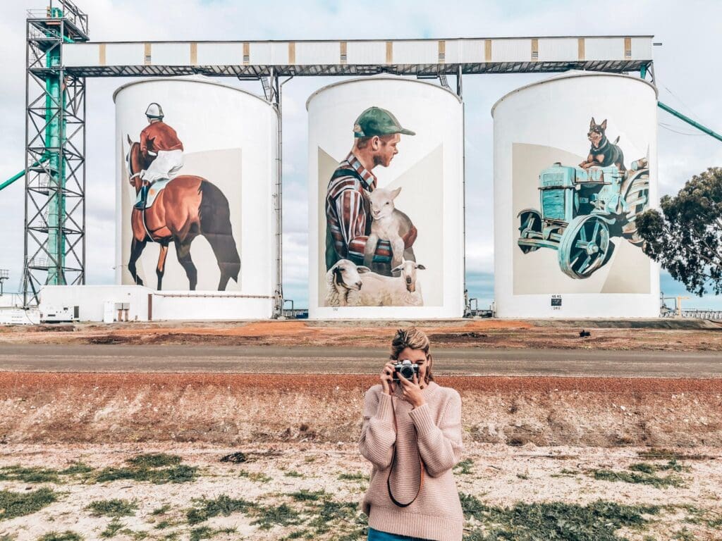 A woman in front of painted grain silos in Pingrup