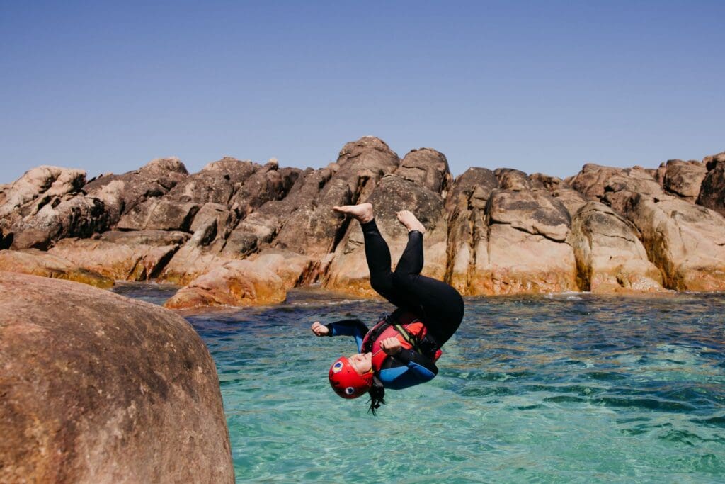 Person in a helmet and wetsuit performing a flip off rocks while on a coasteering experience.